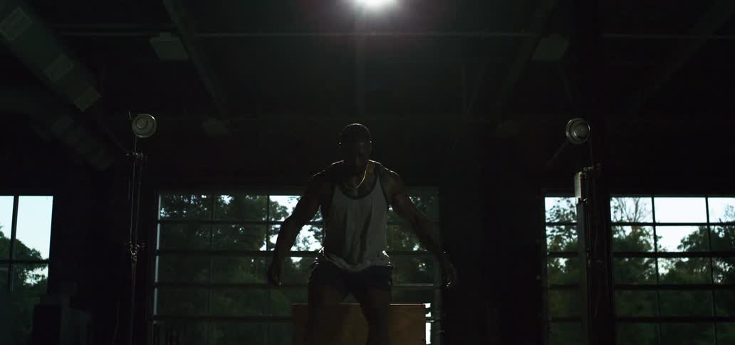 A powerful athlete performs a box jump in super slow motion, silhouetted by a dramatic spotlight in an industrial gym