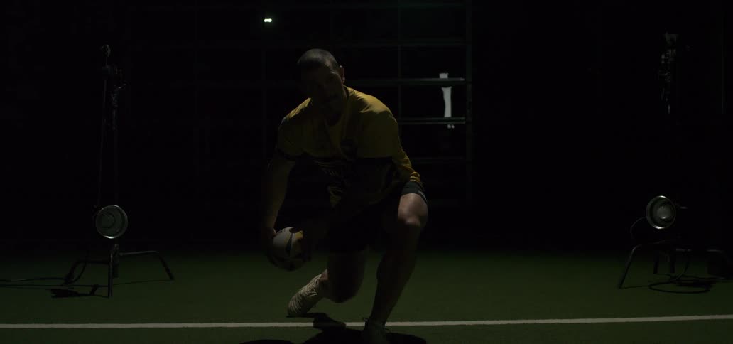 Dramatic slow motion of a powerful rugby player passing the ball in a dark studio with a bright flash of light