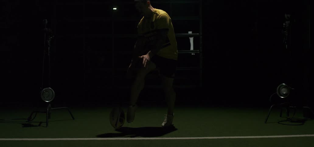 A powerful rugby player executes a perfect drop kick in a dramatically lit studio, captured in stunning super slow motion
