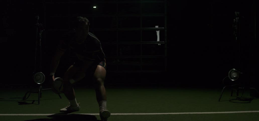 A powerful rugby player passes the ball in a dramatic slow-motion sequence under flashing strobe lights in an indoor training facility