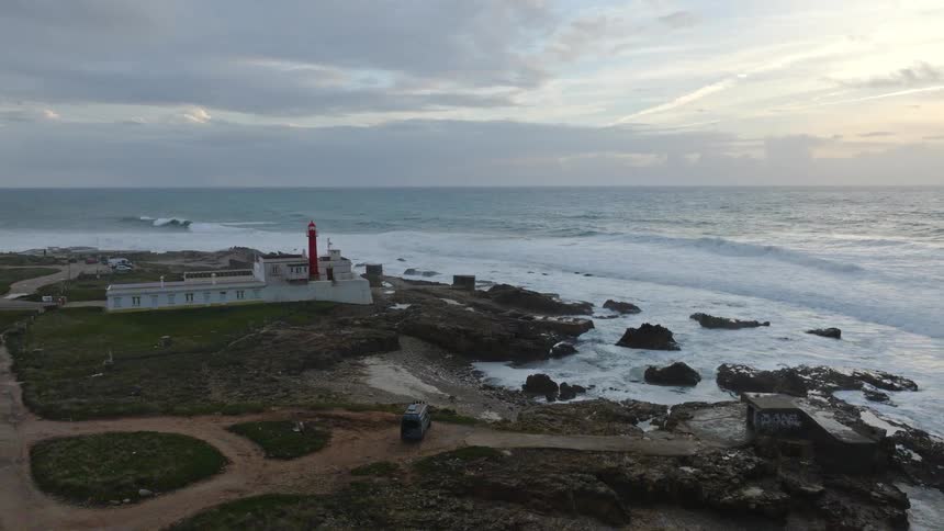 Dramatic aerial view pulling back from a lighthouse on a rocky coastline with large ocean waves crashing on the shore