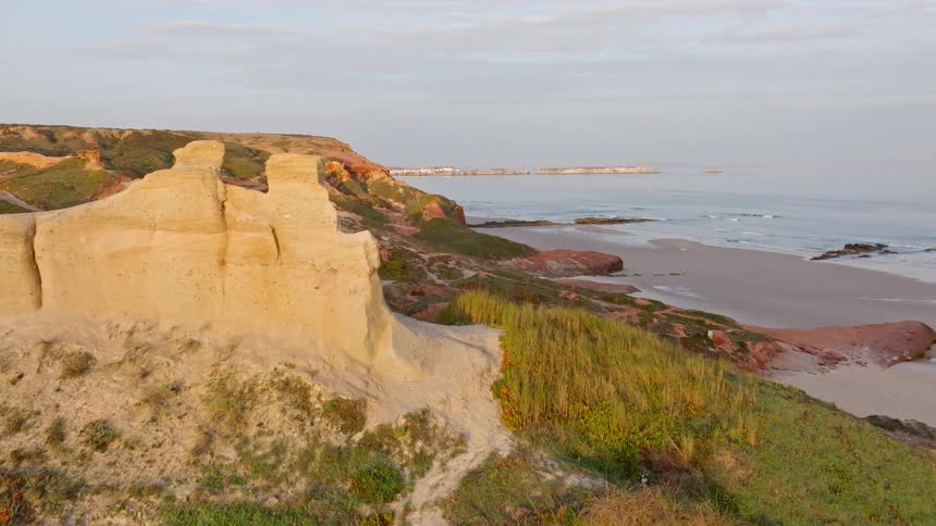 A slow aerial shot reveals the beautiful and rugged coastline with unique rock formations and a sandy beach