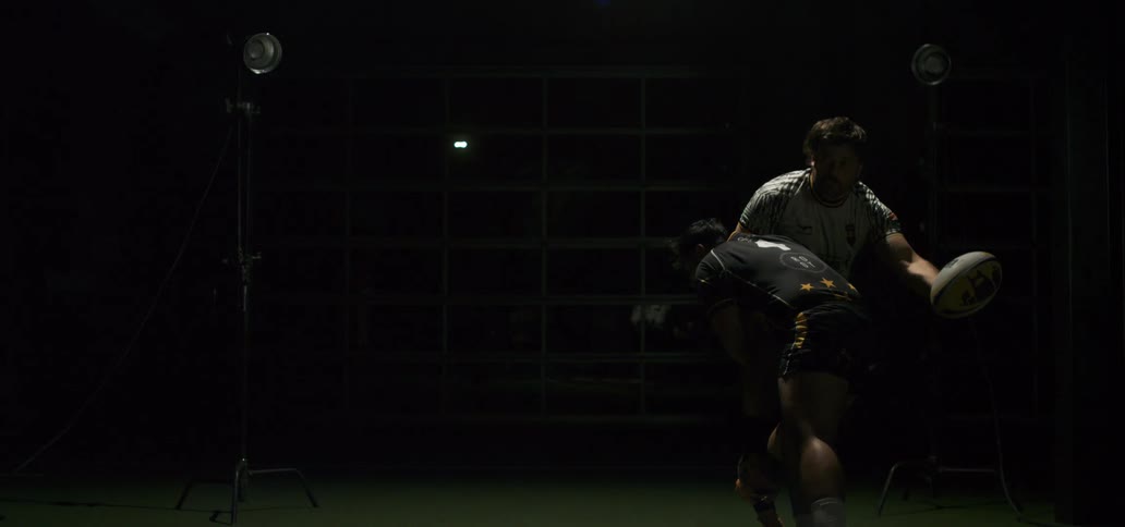 Rugby player gets tackled while throwing a pass in a dramatically lit studio in slow motion