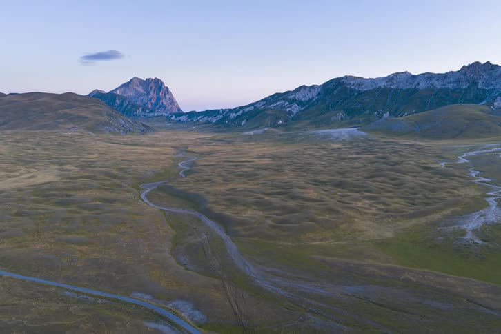 A slow aerial flight over a vast, serene valley towards a distant mountain range glowing in the early morning sunrise