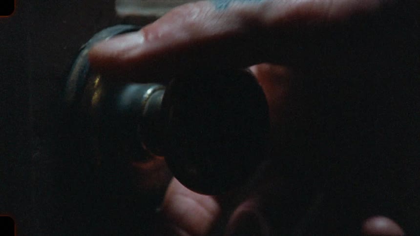 A suspenseful close-up shot on grainy film shows a hand slowly turning a vintage doorknob and opening a door into darkness