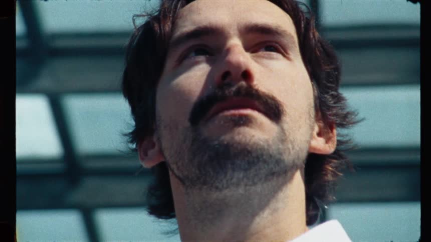 Low angle close-up of a thoughtful man with a mustache looking up towards the light in a vintage, film-style clip