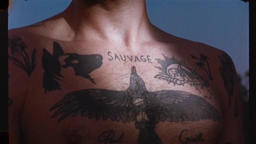 A gritty, vintage film close-up reveals a man's heavily tattooed chest as light moves across his skin