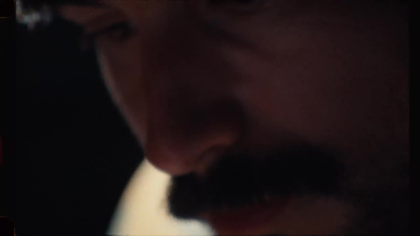 A moody, vintage-style close-up of a tattoo artist's face as he tattoos