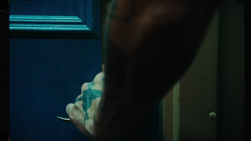 A tattooed hand slowly opens a hotel room door in a dark, moody, vintage-style clip
