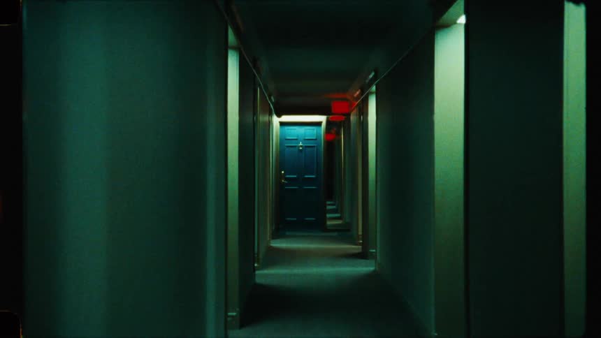 An eerie super 16mm film-style shot slowly pushing down a dark, empty hallway toward a single blue door