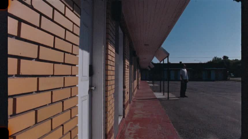 A lone figure stands pensively outside a classic, deserted roadside motel under a clear blue sky