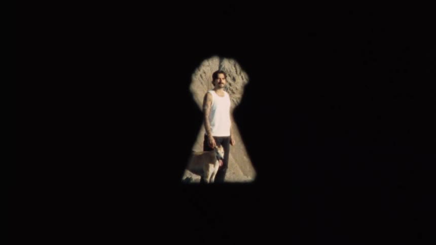 Voyeuristic view through a vintage keyhole reveals a man with a mustache and his dog looking back