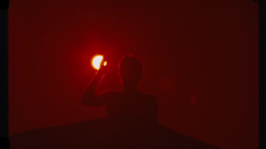 A stunning silhouette shot shows a person seemingly holding the brilliant red sun in their hand during a vibrant sunset