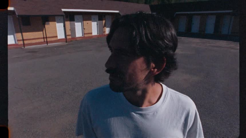 A man walks slowly through a deserted motel parking lot with a pensive expression in this gritty, vintage-style footage