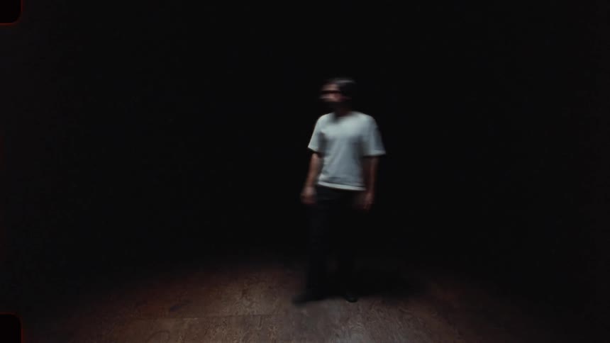 Dreamlike vintage-style footage captures a man in a spotlight, his movements blurred and ethereal in a dark, empty room