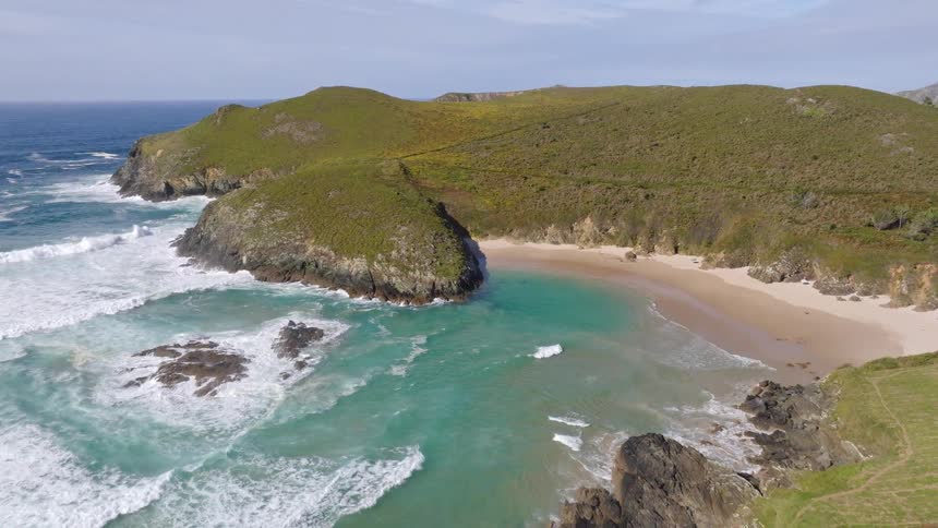 An epic aerial view captures a pristine, secluded beach with turquoise water nestled among rolling green hills