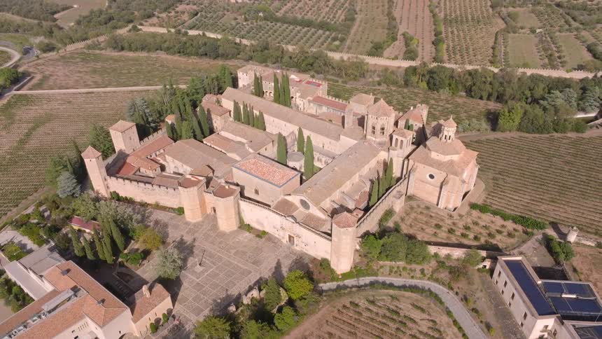 A sweeping high-angle aerial view of the historic Poblet Monastery in Spain, nestled among sprawling vineyards and fields