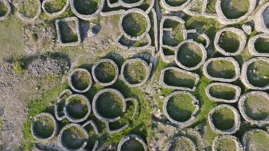 Top-down aerial drone shot slowly pulling up to reveal the magnificent ancient ruins of a Celtic settlement in Spain
