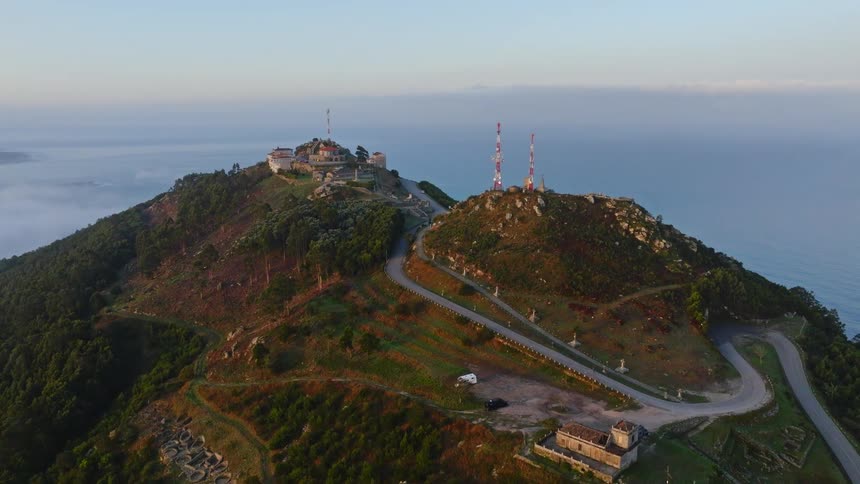 An epic aerial reveal of the ancient Castro de Santa Trega ruins and communication towers on a mountaintop overlooking the misty coastline of Galicia, Spain