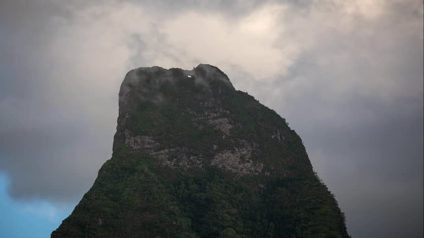 Timelapse of dramatic clouds passing over a lush green tropical mountain peak with a hole at the top