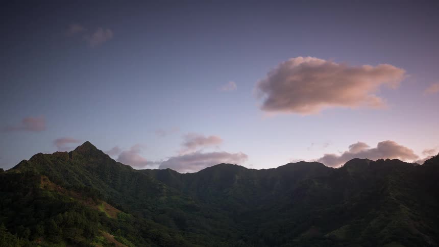 A tranquil time-lapse captures clouds drifting across the sky above a lush mountain range at twilight