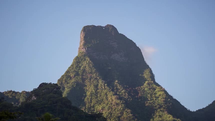 A timelapse captures the shifting light and shadows across the majestic, jungle-covered Mount Mou'a Puta on a clear day