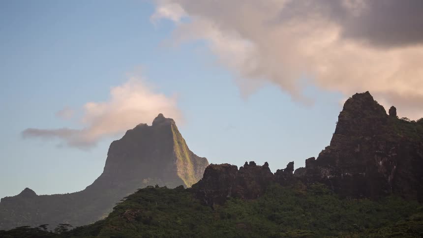 A serene time-lapse shows clouds dancing over the lush, volcanic peaks of a tropical island