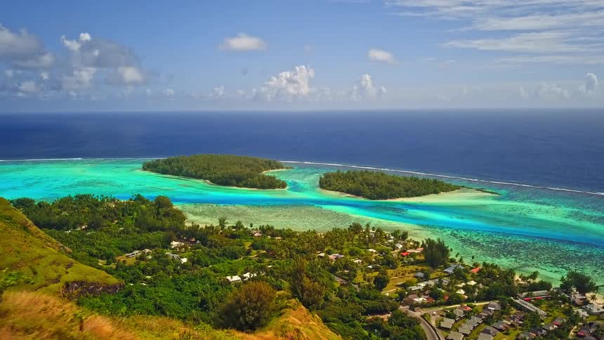 A couple stands on a scenic viewpoint overlooking a stunning tropical island with a vibrant turquoise lagoon and deep blue ocean