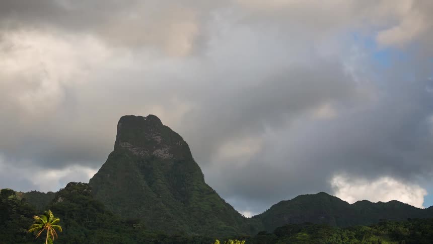 A stunning timelapse of dramatic clouds moving over a sunlit green tropical mountain peak in an island paradise