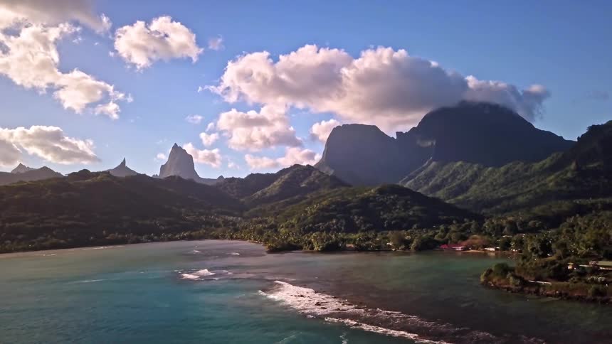 A stunning aerial view of a tranquil tropical bay framed by majestic green mountains under a beautiful blue sky