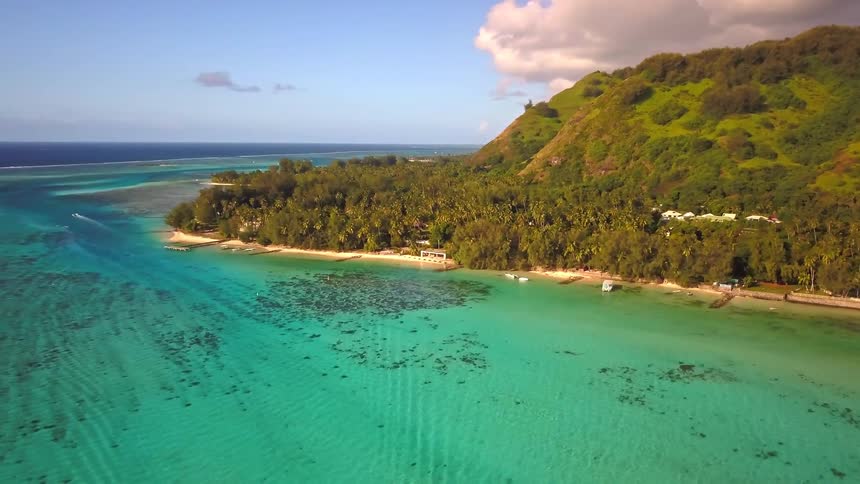 A stunning aerial shot slowly pulls back from a tropical island shoreline revealing a vast turquoise lagoon and lush green mountains