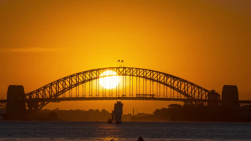 A beautiful timelapse of a golden sunset behind the iconic Sydney Harbour Bridge as boats sail across the water