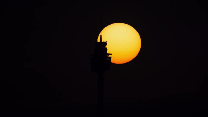 A stunning time-lapse shows a giant orange sun with visible sunspots setting behind the silhouetted Sydney Tower