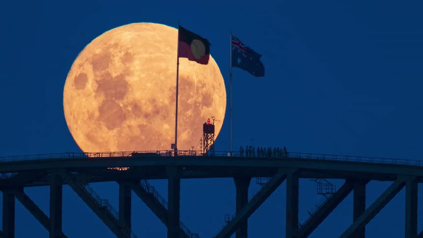 A stunning time-lapse shows a huge, orange full moon rising behind the Sydney Harbour Bridge, with the Aboriginal and Australian flags waving at the summit