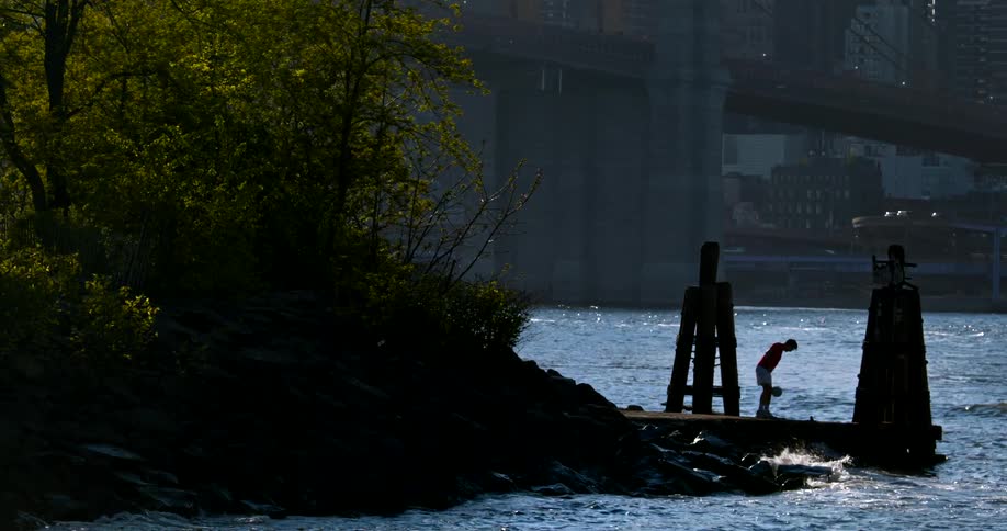 A man juggles a soccer ball on a pier in slow motion with the Brooklyn Bridge in the background