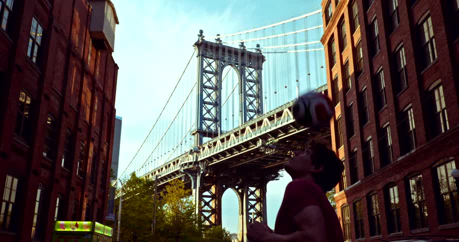 Cinemagraph of a silhouetted man skillfully heading a soccer ball on a DUMBO street with the Manhattan Bridge towering in the background