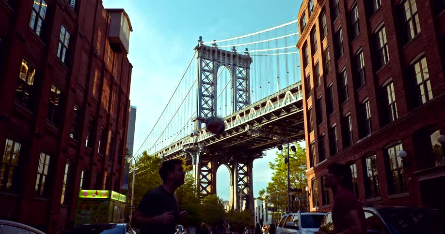 Two athletic men in slow motion pass a soccer ball back and forth with their heads on a classic DUMBO street with the Manhattan Bridge centered in the background
