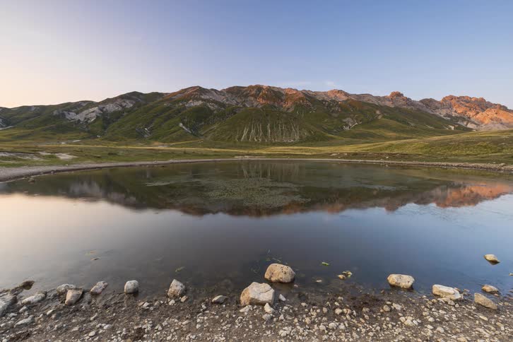 A serene timelapse captures the reflection of a majestic mountain range in a still alpine lake as the light fades at dusk