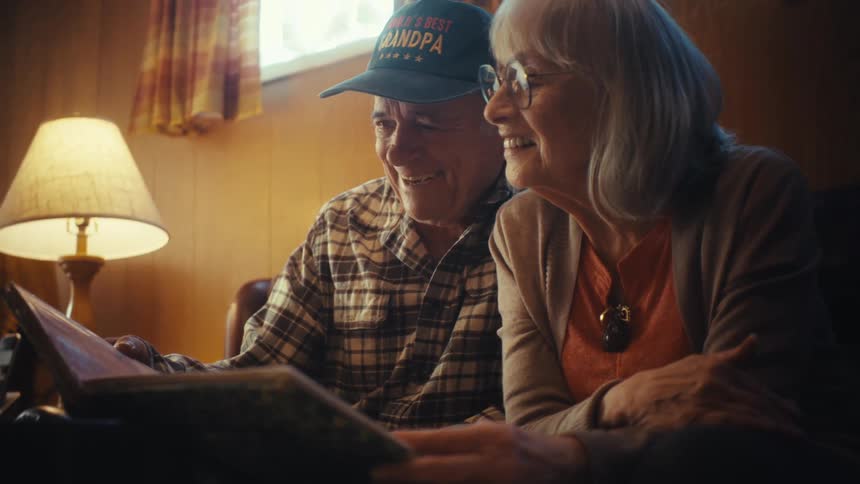 An elderly couple smiles warmly while looking through a photo album together in their cozy living room