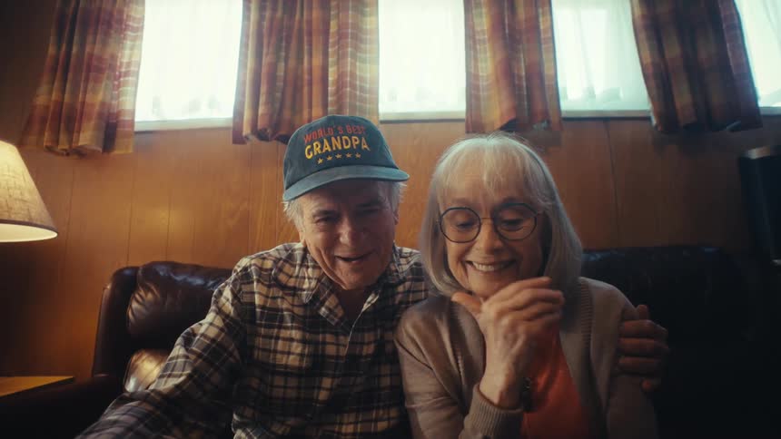 A loving senior couple smiles and gets sentimental while reminiscing over old photos in a photo album at home