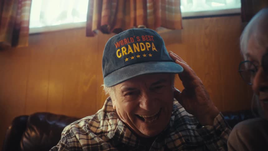 A heartwarming, slow-motion close-up of an elderly couple smiling and laughing as they look through an old family photo album together
