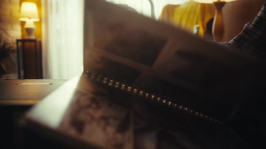 Elderly hands slowly turn the fragile pages of a photo album, lost in the nostalgic warmth of cherished memories