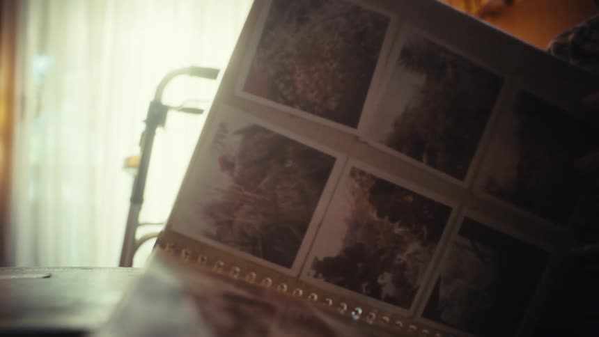 An elderly person with a walker nearby slowly turns the pages of an old photo album, reminiscing about the past
