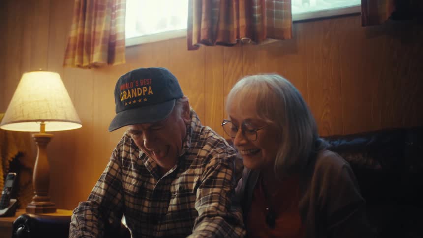 An elderly couple joyfully reminisces over old memories while looking through a photo album together in their cozy living room