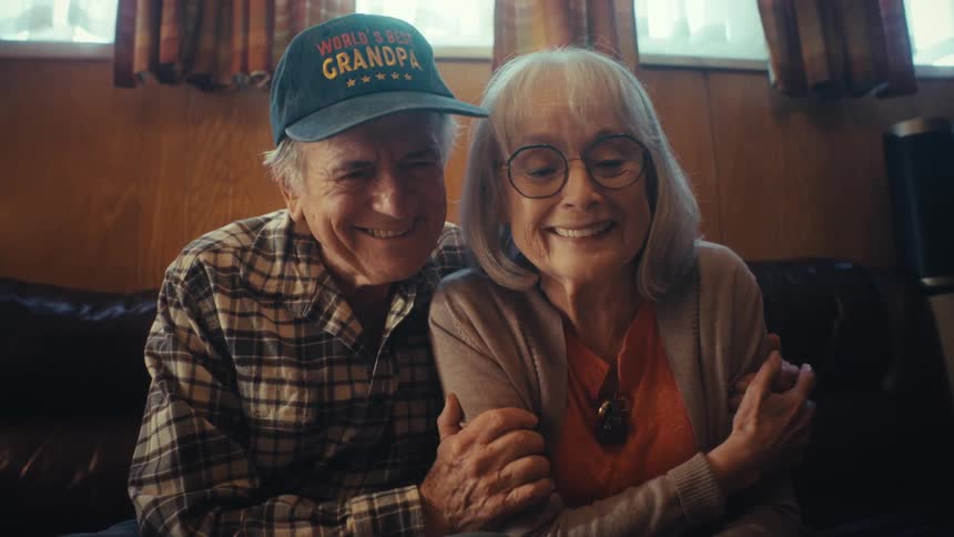A loving elderly couple reminisces as they look through a photo album, sharing smiles and a tender embrace on their couch