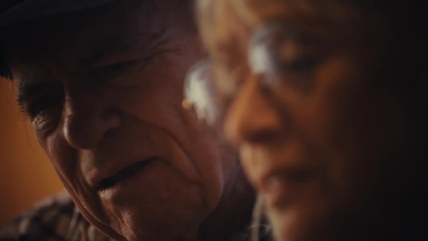 An intimate close-up shows an elderly couple having a serious conversation, with the camera slowly shifting focus from the man to the woman