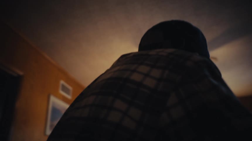 An elderly man with a walker smiles warmly as he walks through a doorway into the living room where his wife is waiting