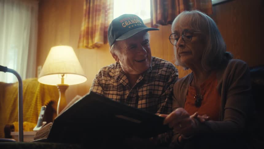 A nostalgic senior couple smiles while looking through a photo album together in their cozy living room