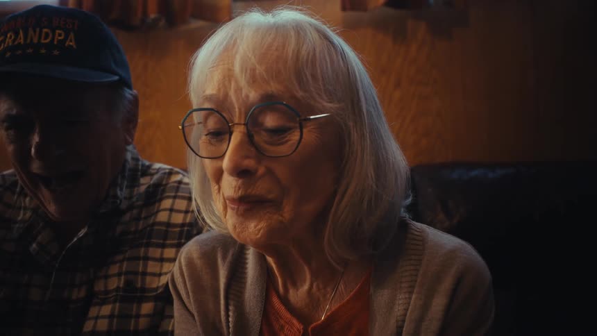 A heartwarming slow-motion close-up of an elderly couple sharing a laugh that turns into an emotional, touching moment for the grandmother
