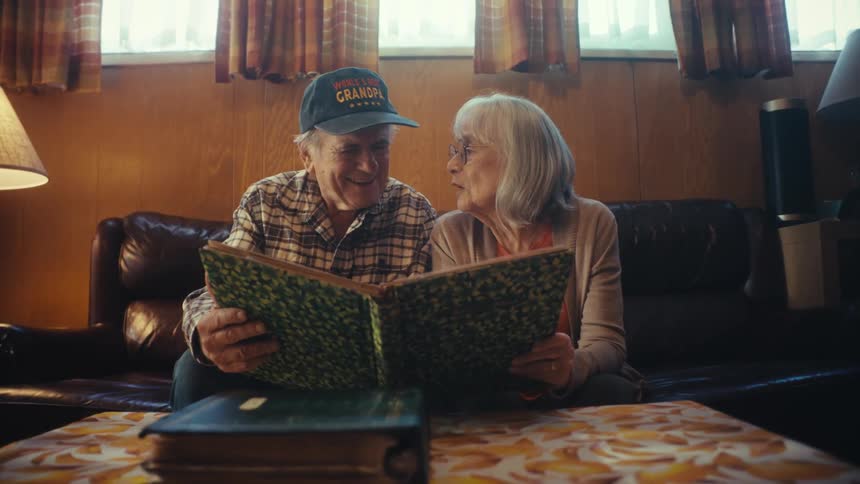 An elderly couple smiles and reminisces while looking through a photo album together in their cozy living room